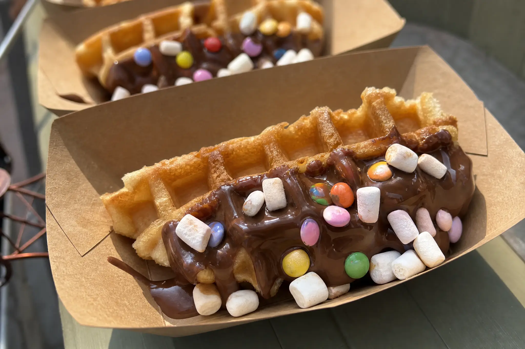 Waffeln am Stiel mit Schokolade und bunten Toppings in Pappschalen