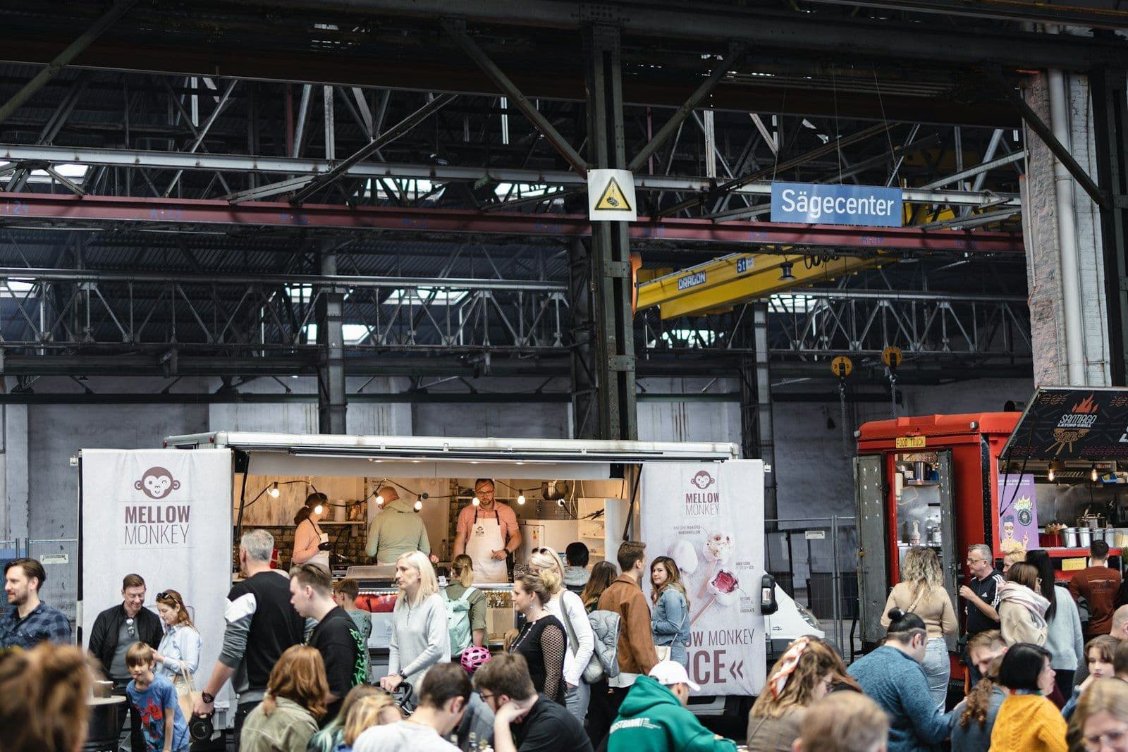 Gäste an Bierbänken in einer Halle mit Essensständen